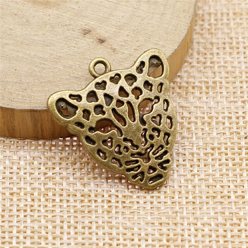 Handmade leopard head pendant in antique bronze finish on wooden background for DIY jewelry accessories.