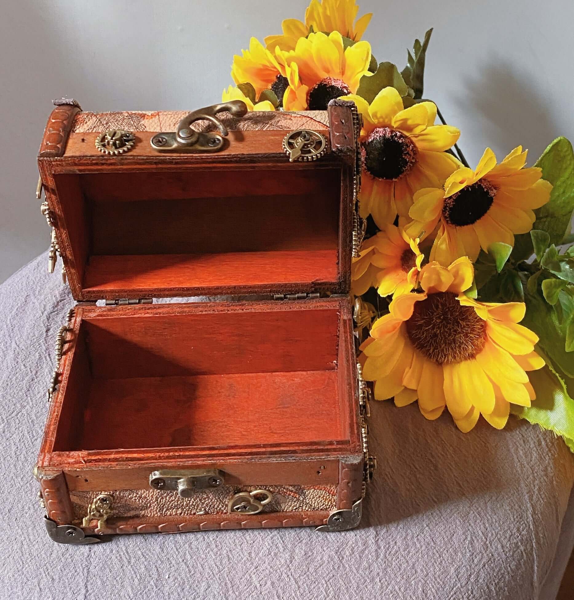 Handmade wooden storage box with steampunk design, open and surrounded by sunflowers.