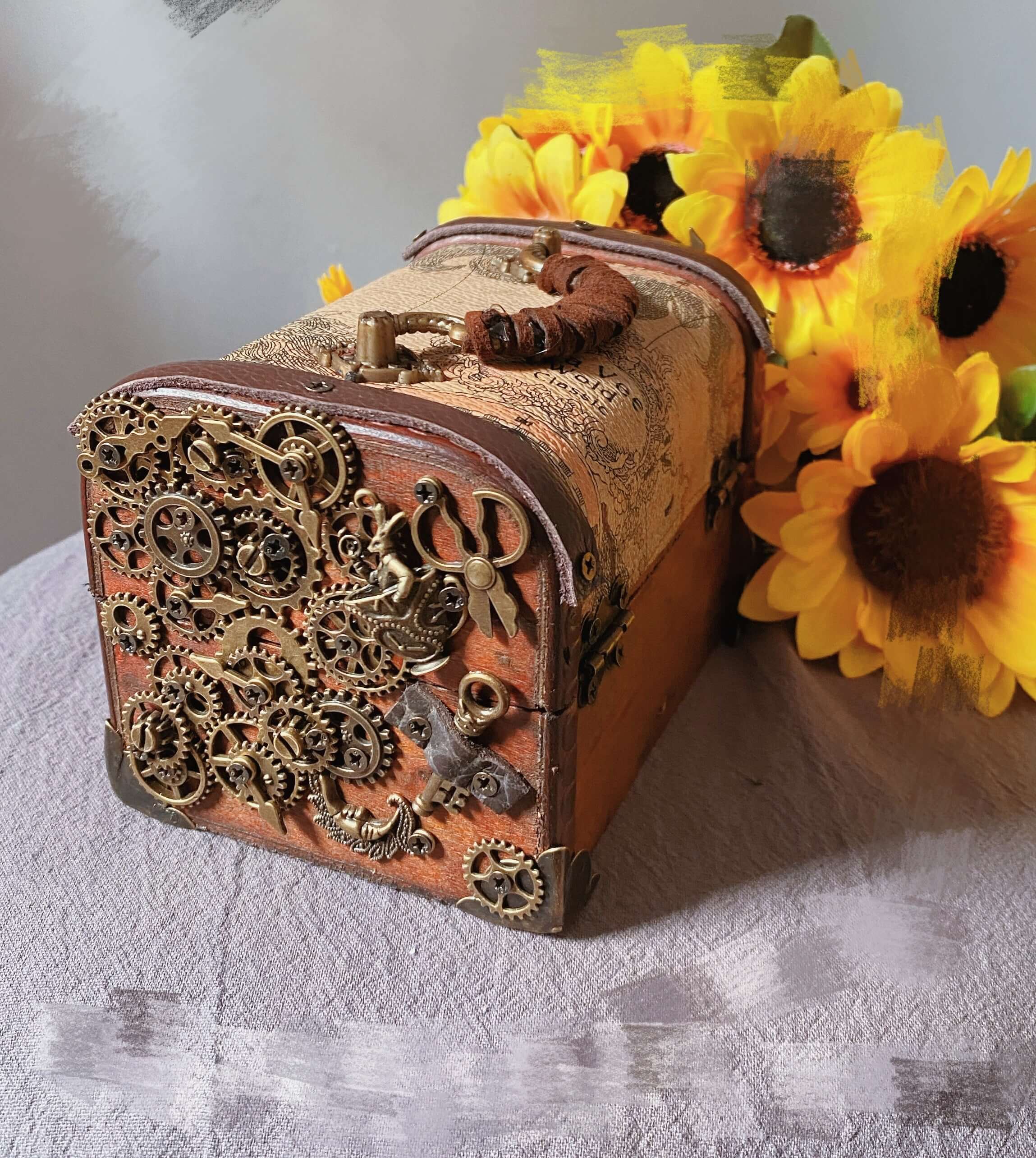 Handmade steampunk jewelry wooden box adorned with gears and lace, beside vibrant sunflowers.