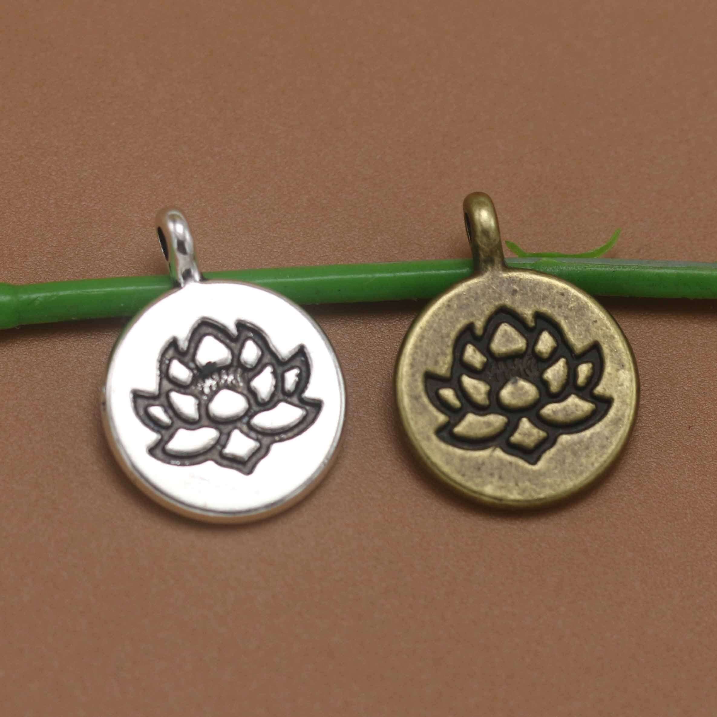 Vintage alloy lotus pendants in silver and bronze sitting on a green stem against a brown background.