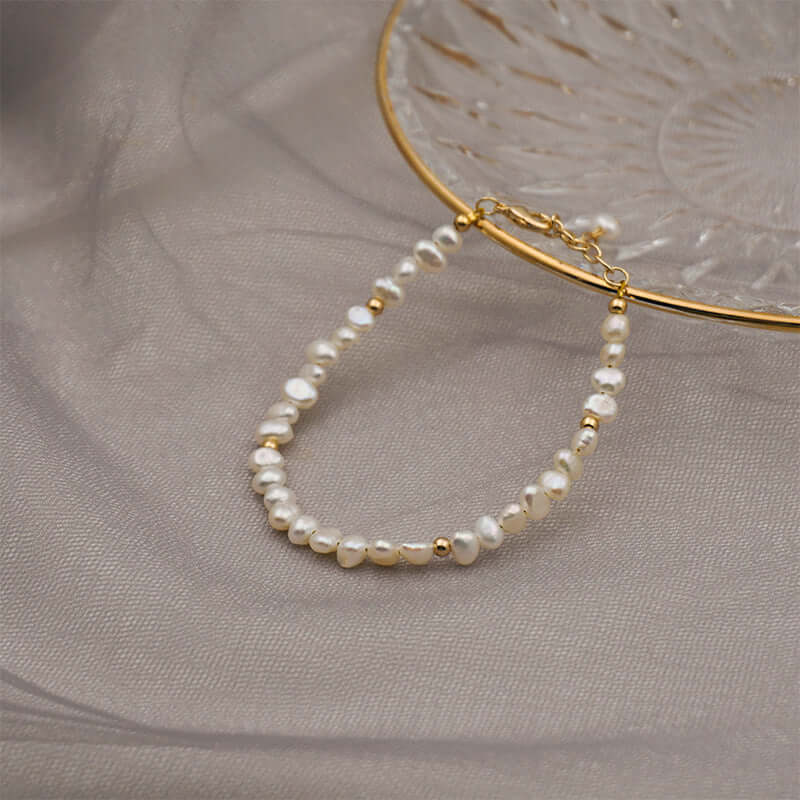 Handmade baroque pearl bracelet with gold accents, elegant jewelry on textured fabric background.