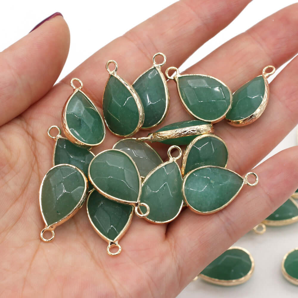 Collection of green Dongling jade drop-shaped pendants with gold accents, held in a hand.
